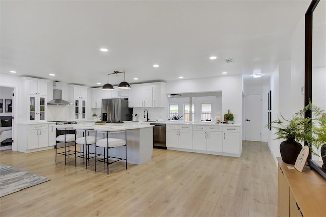 kitchen featuring visible vents, wall chimney exhaust hood, a center island, stainless steel appliances, and light wood-type flooring