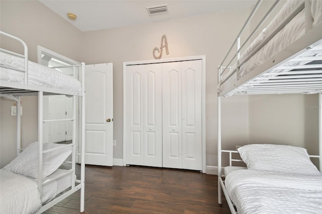 bedroom with baseboards, visible vents, dark wood finished floors, and a closet