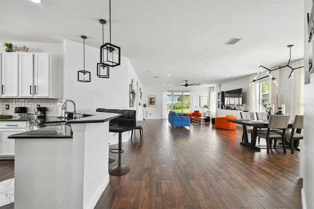 kitchen with dark wood-style floors, dark countertops, visible vents, decorative backsplash, and a sink