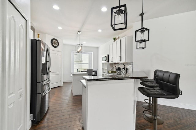 kitchen featuring dark wood finished floors, a breakfast bar, a peninsula, stainless steel appliances, and a sink