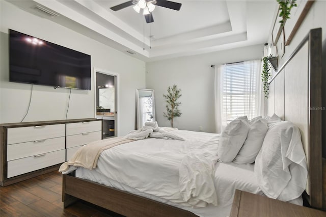 bedroom with dark wood-style floors, visible vents, a tray ceiling, and ceiling fan