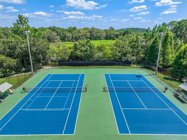 view of tennis court with a forest view and fence