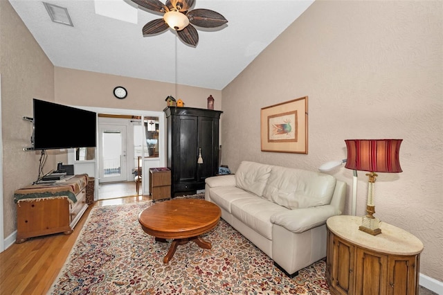 living room with light wood-type flooring, a ceiling fan, baseboards, vaulted ceiling, and a textured wall