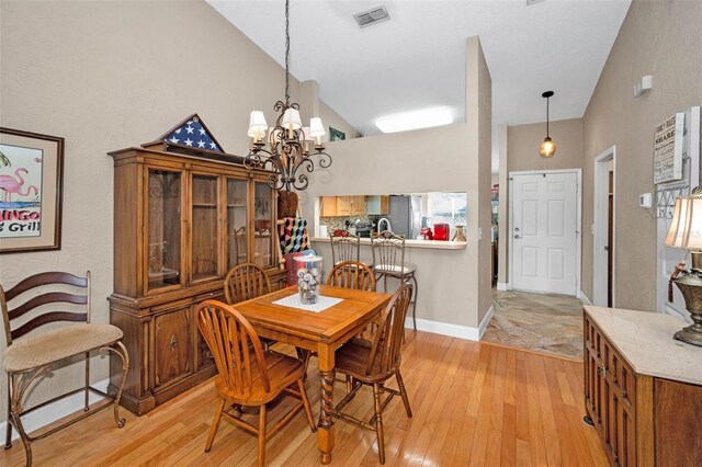 dining space featuring visible vents, light wood-style floors, a chandelier, and high vaulted ceiling