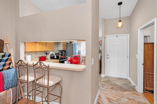 kitchen with a kitchen breakfast bar, stainless steel appliances, light countertops, decorative backsplash, and baseboards