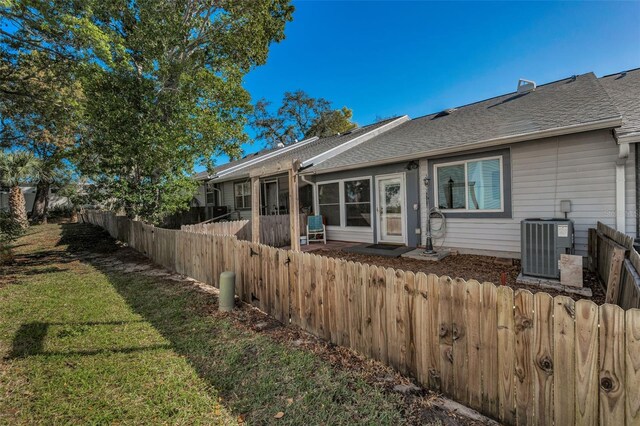 view of front of property featuring a front yard, central AC unit, fence, and a shingled roof