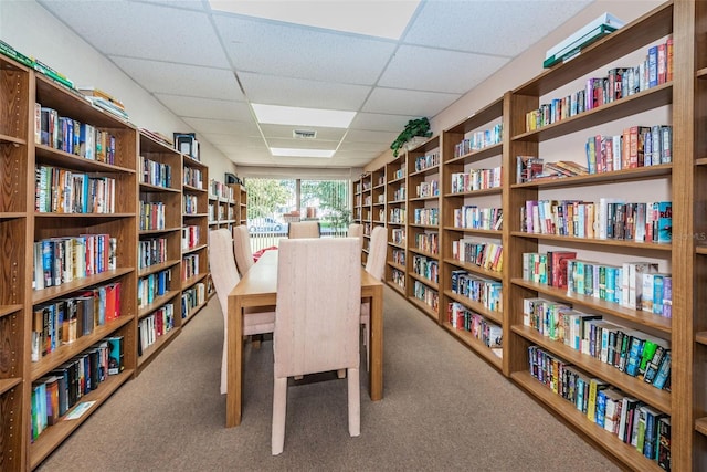 carpeted office space with wall of books, visible vents, and a drop ceiling