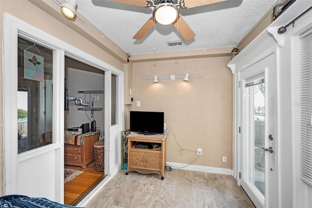 living area featuring baseboards, a textured ceiling, visible vents, and a ceiling fan