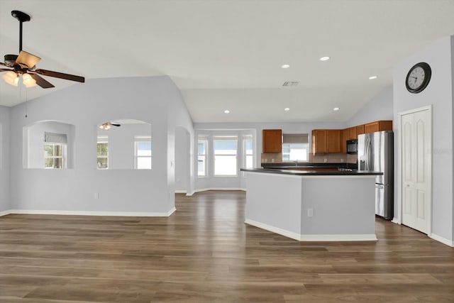 kitchen with open floor plan, vaulted ceiling, stainless steel refrigerator with ice dispenser, brown cabinets, and dark countertops