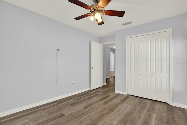 unfurnished bedroom with baseboards, visible vents, arched walkways, wood finished floors, and a closet