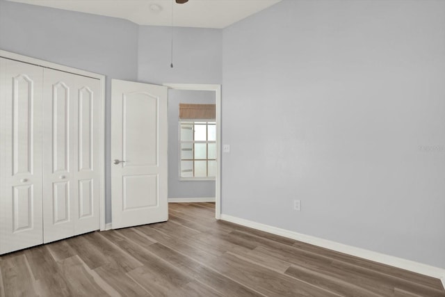 unfurnished bedroom featuring wood finished floors, a ceiling fan, baseboards, vaulted ceiling, and a closet