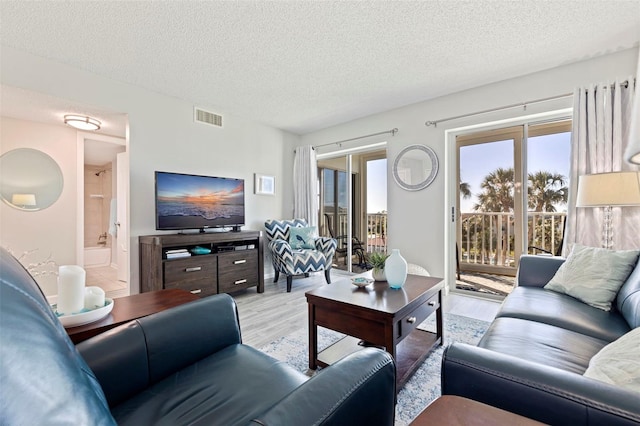 living area featuring a textured ceiling, light wood-type flooring, visible vents, and a healthy amount of sunlight