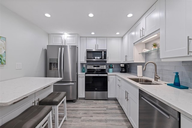 kitchen featuring tasteful backsplash, white cabinets, appliances with stainless steel finishes, light stone countertops, and a sink