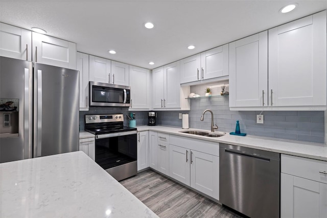 kitchen with a sink, white cabinetry, appliances with stainless steel finishes, light wood finished floors, and tasteful backsplash