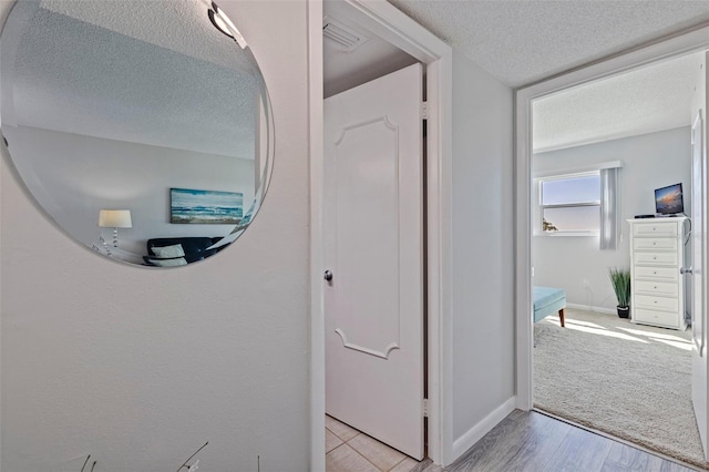 hallway featuring a textured ceiling, light wood-style flooring, light carpet, visible vents, and baseboards