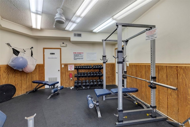 exercise area with wooden walls, a wainscoted wall, visible vents, and a textured ceiling