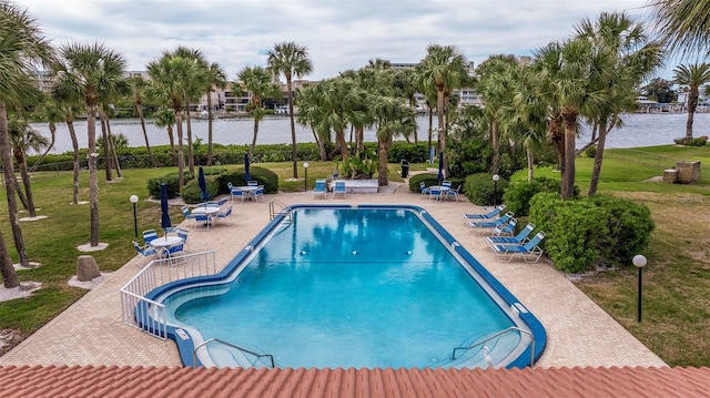 pool featuring a patio area, a water view, a yard, and fence