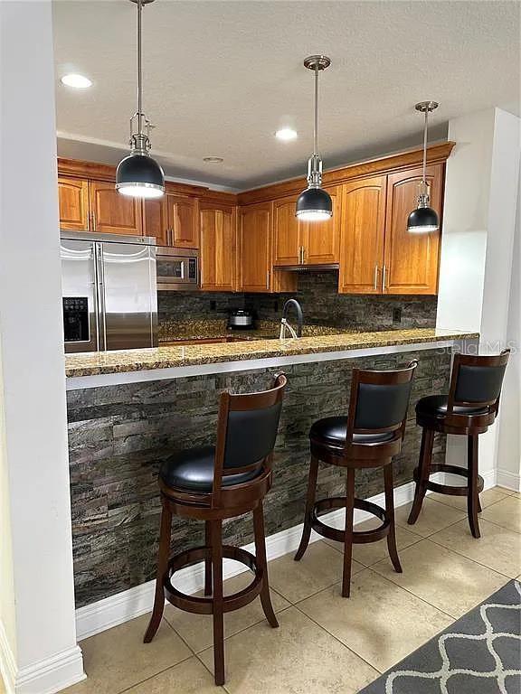 kitchen with brown cabinetry, a breakfast bar area, built in appliances, pendant lighting, and backsplash