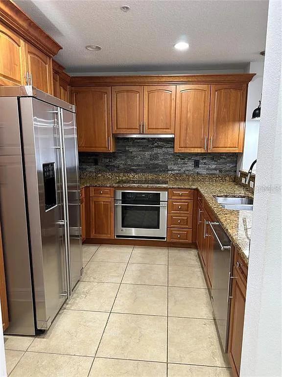 kitchen with light tile patterned floors, brown cabinetry, dark stone countertops, stainless steel appliances, and a sink