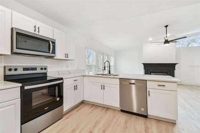 kitchen featuring appliances with stainless steel finishes, white cabinets, a sink, ceiling fan, and a peninsula