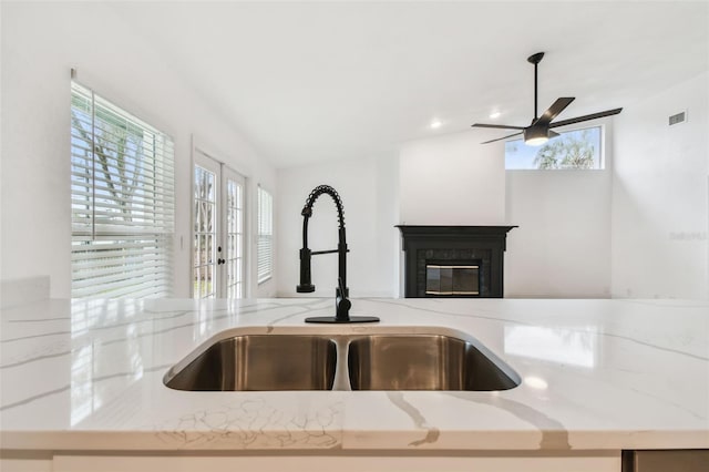 room details featuring visible vents, a ceiling fan, a glass covered fireplace, a sink, and light stone countertops