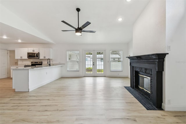 unfurnished living room with french doors, a fireplace with flush hearth, light wood-style floors, vaulted ceiling, and baseboards
