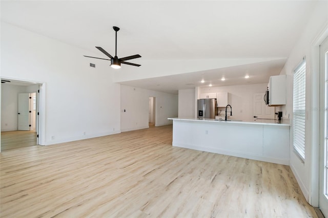 unfurnished living room with lofted ceiling, a sink, visible vents, and light wood-style floors