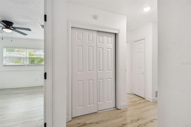 hallway with light wood-style floors, visible vents, and baseboards