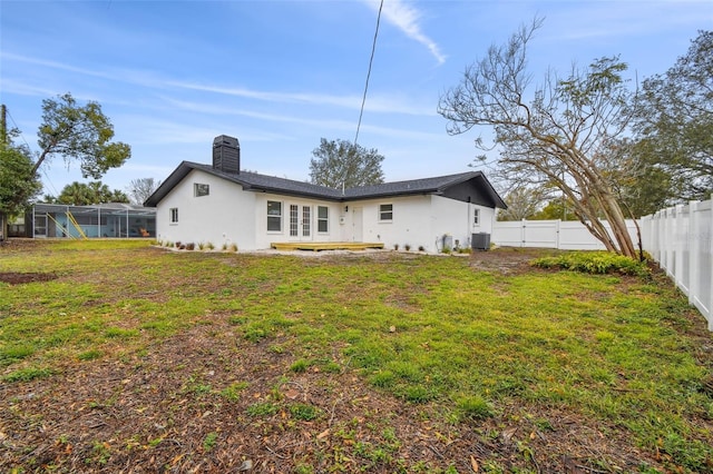 rear view of property featuring glass enclosure, a fenced backyard, central air condition unit, a yard, and a chimney