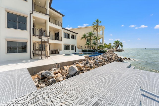 view of patio / terrace featuring a view of the beach, a water view, stairs, and a hot tub