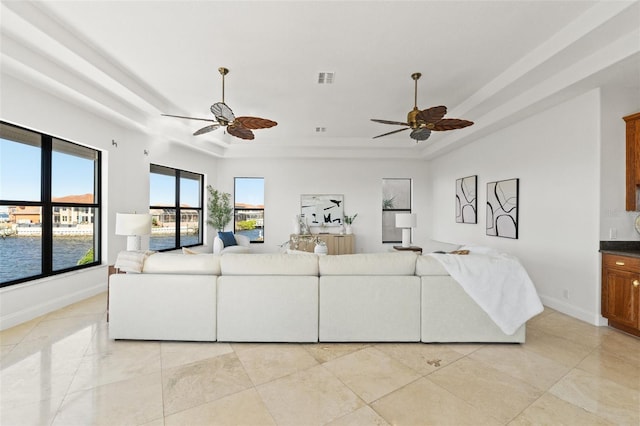 living room featuring a tray ceiling, baseboards, visible vents, and ceiling fan