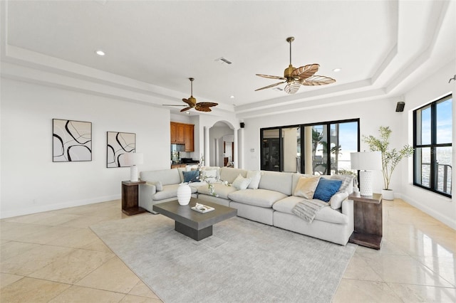 living area with visible vents, ceiling fan, baseboards, arched walkways, and a raised ceiling