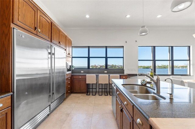 kitchen with crown molding, light tile patterned floors, brown cabinets, stainless steel appliances, and a sink