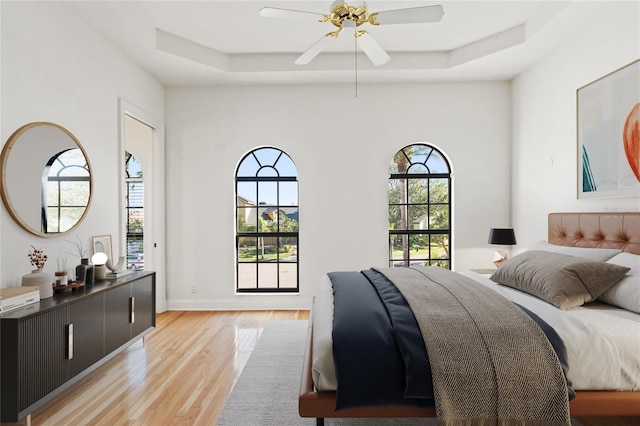 bedroom with multiple windows, a raised ceiling, and light wood-style floors