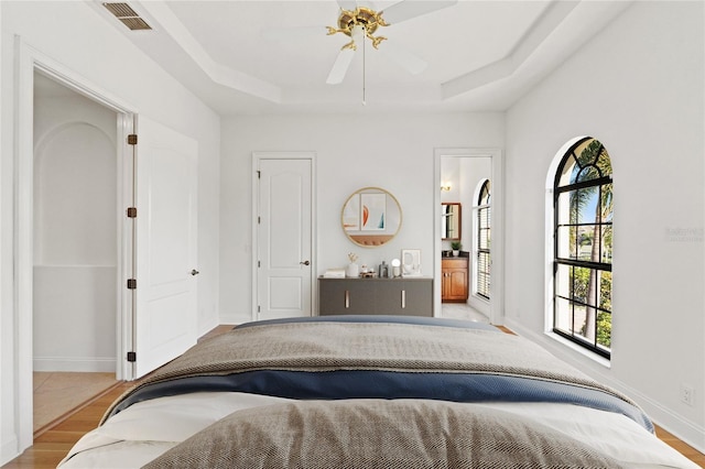 bedroom featuring visible vents, baseboards, a tray ceiling, and wood finished floors