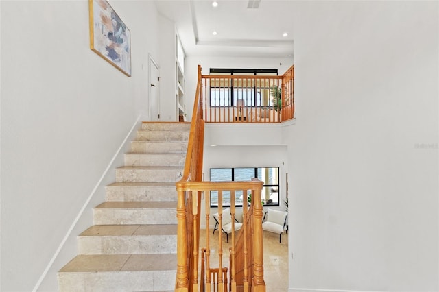 stairway with recessed lighting, a healthy amount of sunlight, baseboards, and a towering ceiling