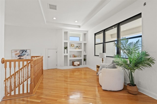 sitting room with visible vents, an upstairs landing, built in features, light wood finished floors, and a raised ceiling