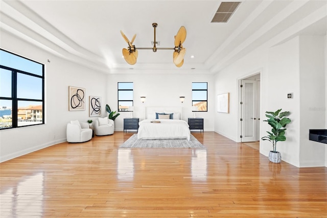 bedroom with visible vents, a raised ceiling, baseboards, and light wood-style flooring