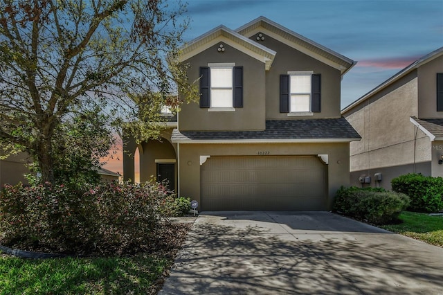 traditional home with driveway, a shingled roof, a garage, and stucco siding