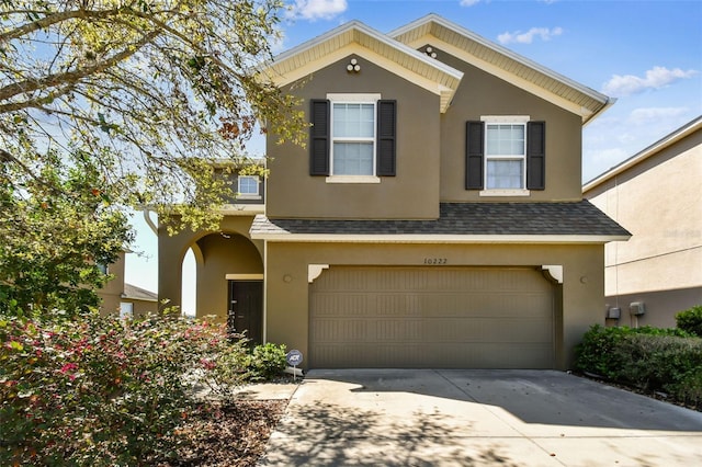 view of front facade featuring a shingled roof, concrete driveway, an attached garage, and stucco siding