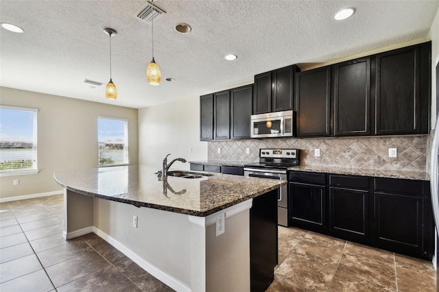 kitchen with tasteful backsplash, a center island with sink, appliances with stainless steel finishes, dark stone countertops, and a sink