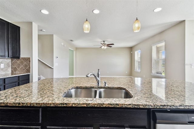 kitchen featuring dark cabinets, decorative light fixtures, a sink, and backsplash