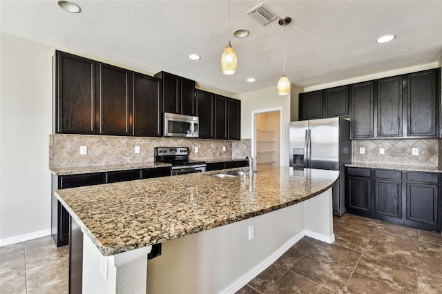 kitchen featuring light stone counters, a kitchen island with sink, stainless steel appliances, a sink, and visible vents