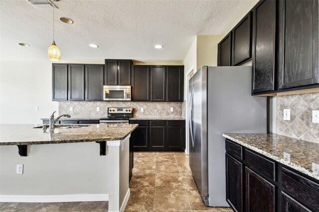 kitchen with stainless steel appliances, a sink, dark stone counters, a kitchen bar, and pendant lighting