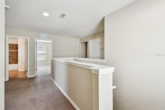 hallway with an upstairs landing, baseboards, visible vents, and carpet flooring