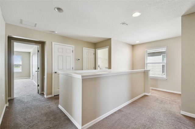 hallway with a textured ceiling, an upstairs landing, visible vents, baseboards, and carpet