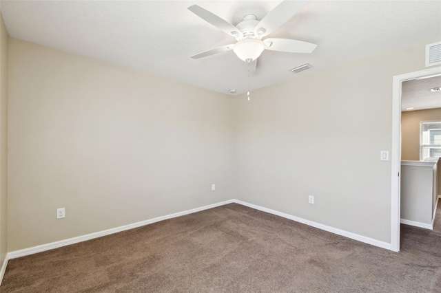 spare room featuring a ceiling fan, dark carpet, visible vents, and baseboards