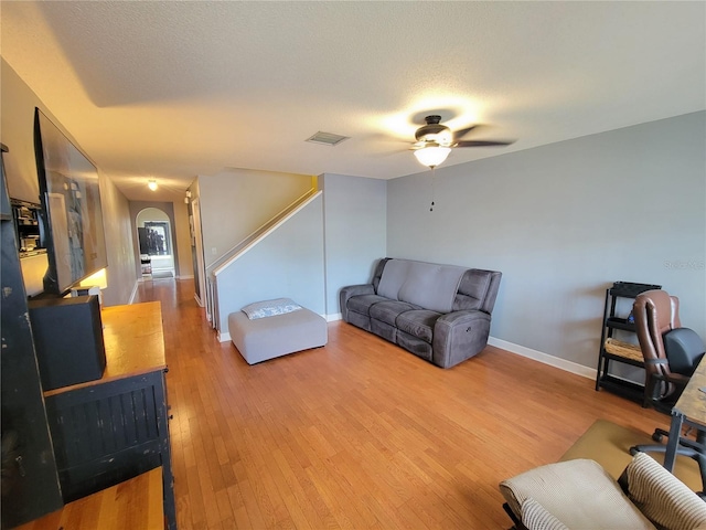 living room with visible vents, arched walkways, baseboards, a textured ceiling, and light wood-type flooring