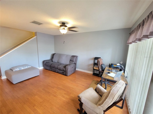 home office featuring visible vents, baseboards, a ceiling fan, light wood-style flooring, and a textured ceiling