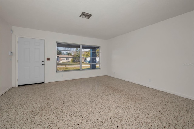 empty room with speckled floor, visible vents, and baseboards